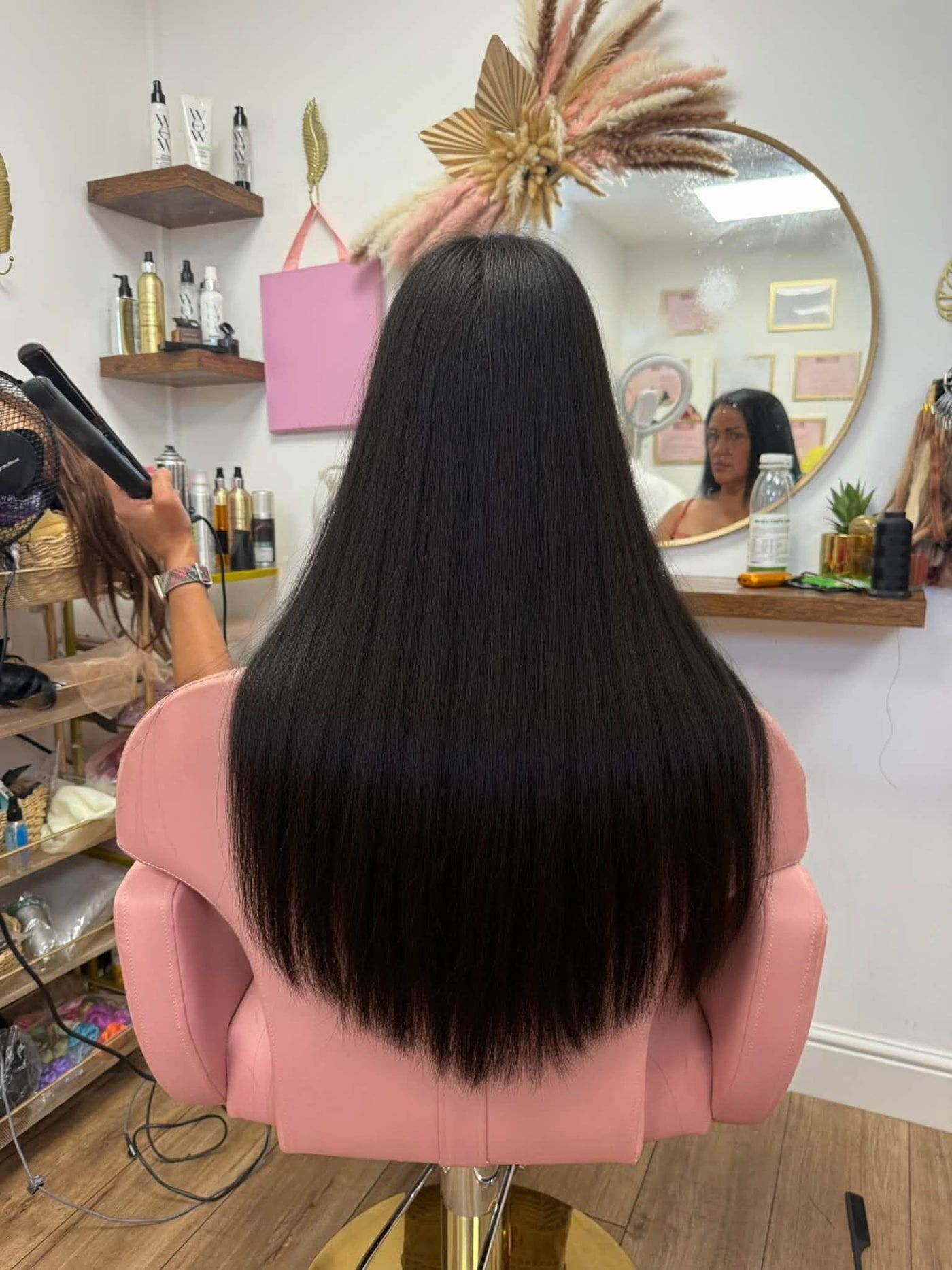 Long, sleek, glossy black hair extensions on a client in Lisa’s pink salon chair